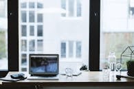 办公桌上摆放着笔记本电脑和一杯水，窗户敞开着，显得很时尚