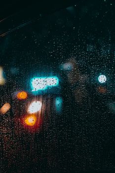 Raindrops on a window create a bokeh effect with city lights at night.