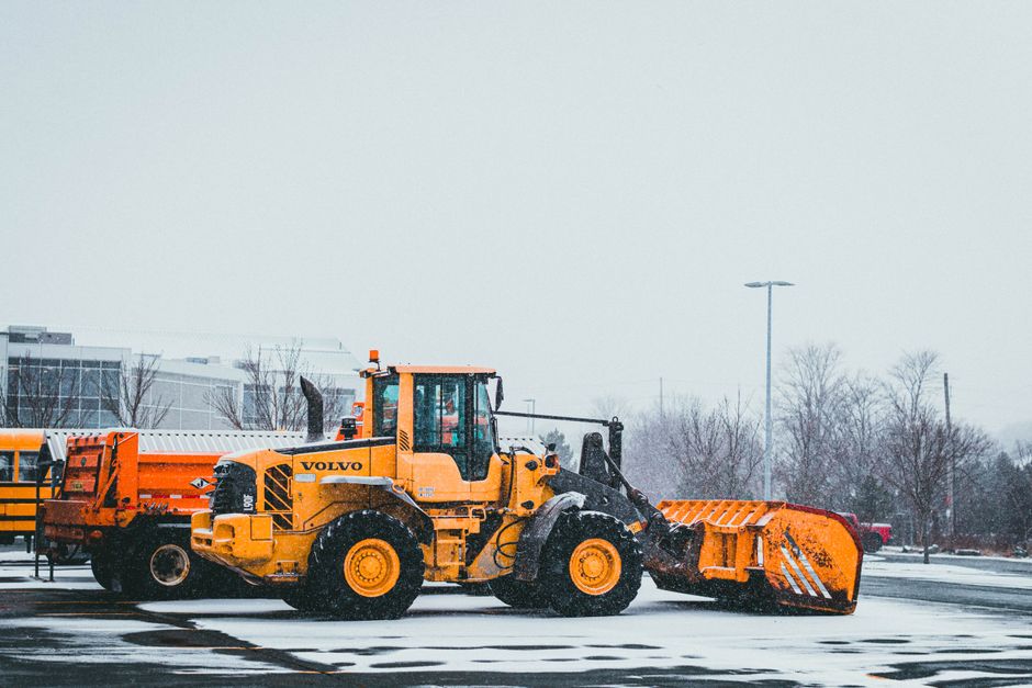 Commercial snow removal equipment clearing a business parking lot at sunrise - commercial landscaping maintenance
