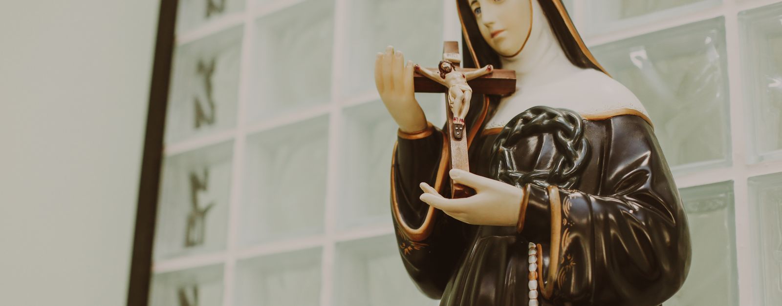 Statue of religious saint holding crucifix indoors, symbolizing faith and devotion.