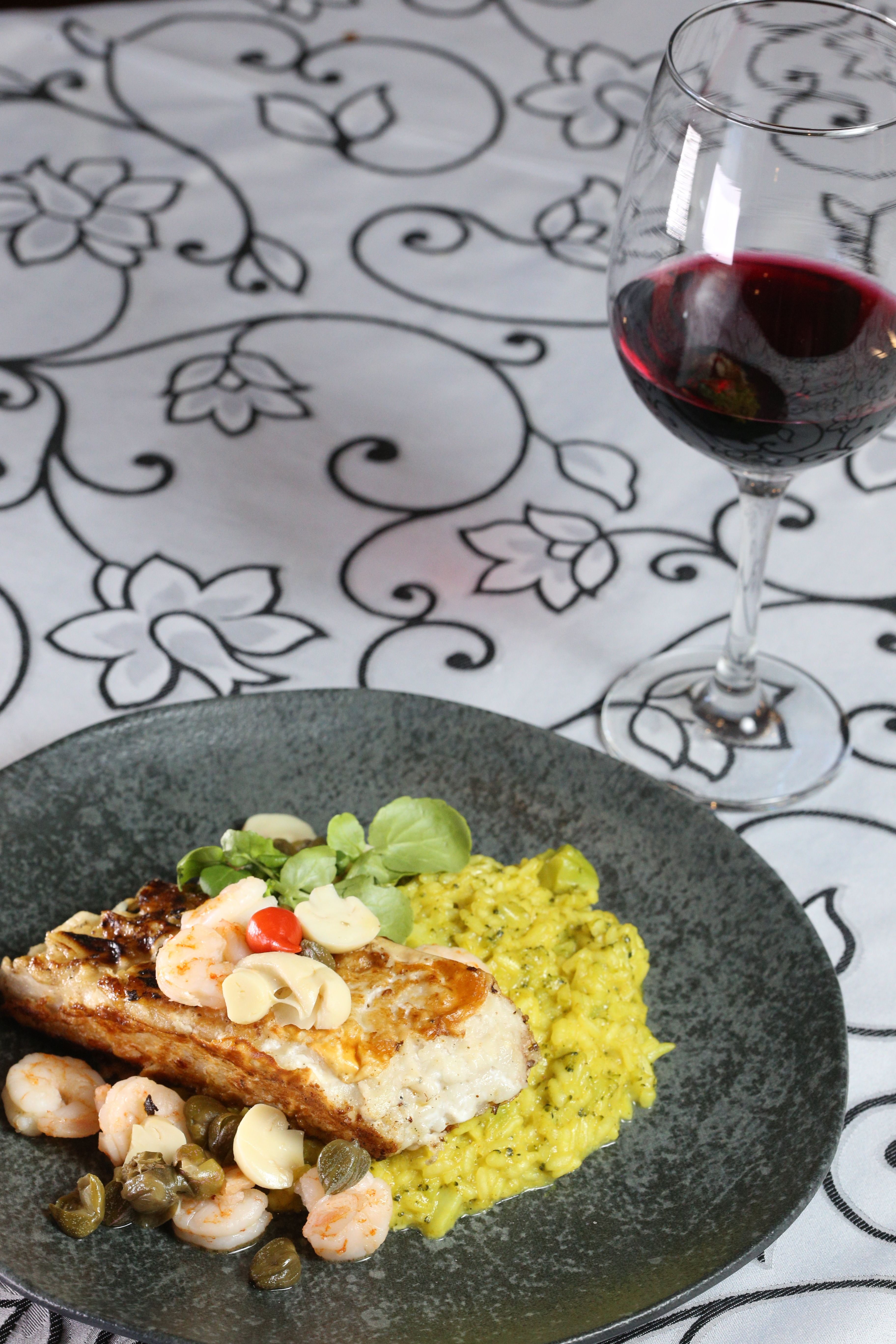 Grilled fish with shrimp and risotto served with red wine, perfect for a gourmet dining experience.