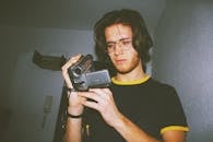 一位戴眼镜的年轻人在室内专注地用老式摄像机录音