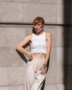 Woman in White Tank Top Leaning on Gray Concrete Wall