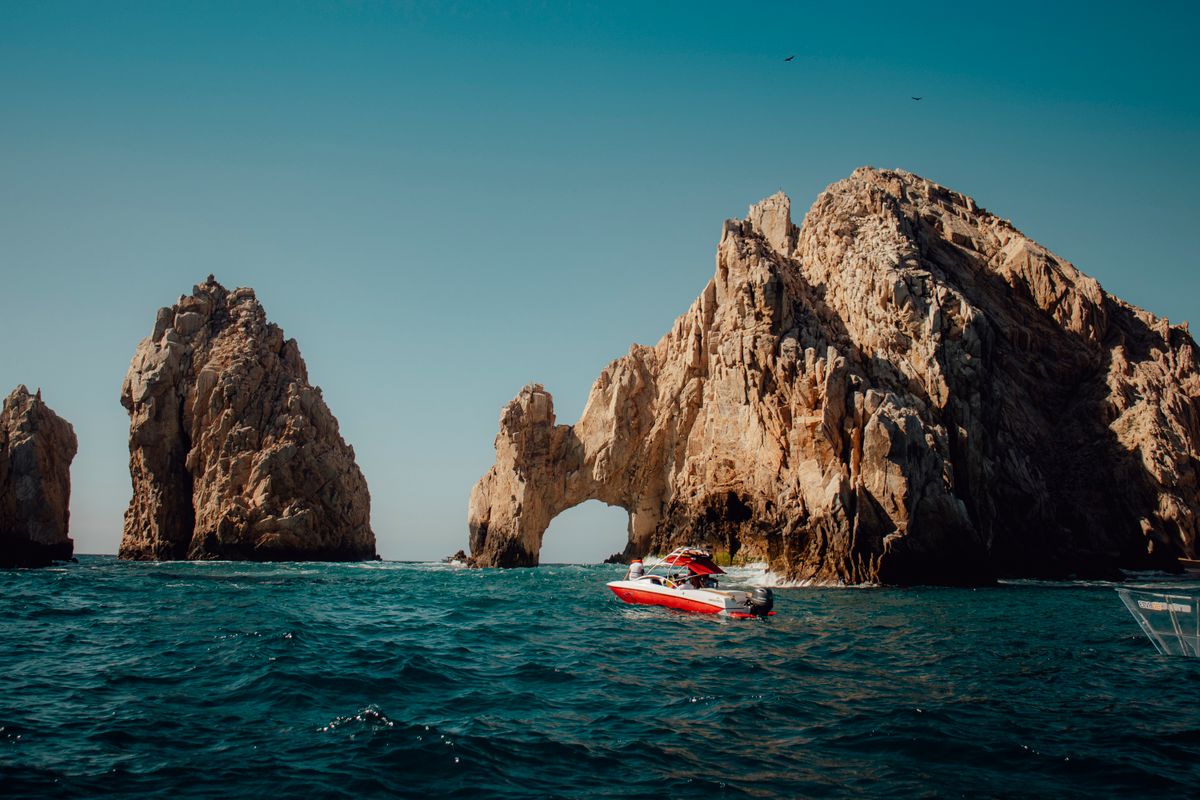 Explore the iconic El Arco rock formations in Cabo San Lucas with a boat navigating the blue Pacific waters.