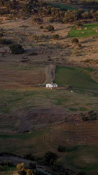 Aerial view of a rural farmhouse surrounded by fields and hills, highlighting serene countryside landscape.