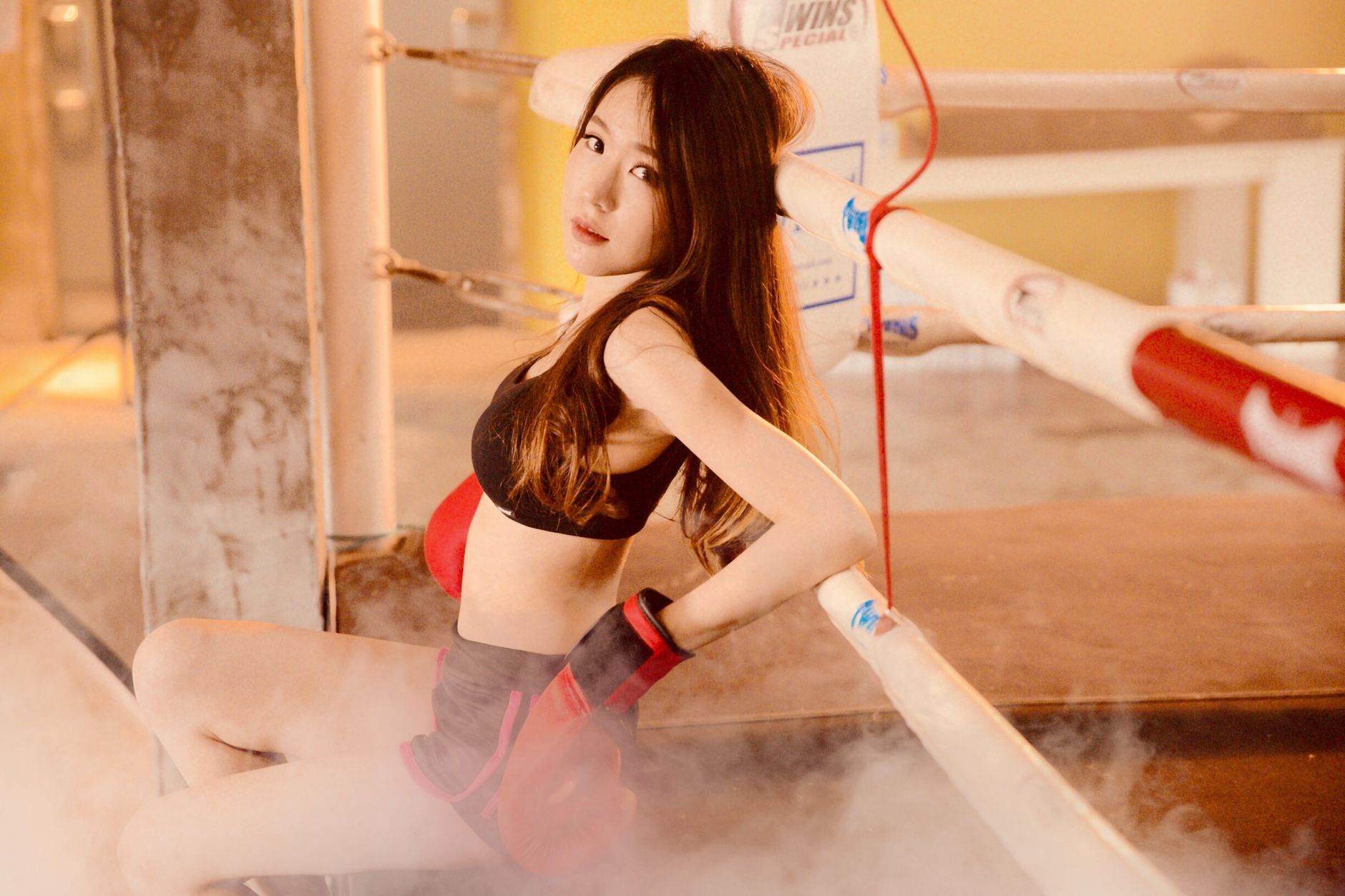 A young woman resting in a boxing ring wearing gloves, exuding strength and focus.