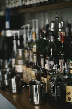 Assorted liquor bottles and glasses in a dimly lit bar setting, showcasing a diverse range of beverages.