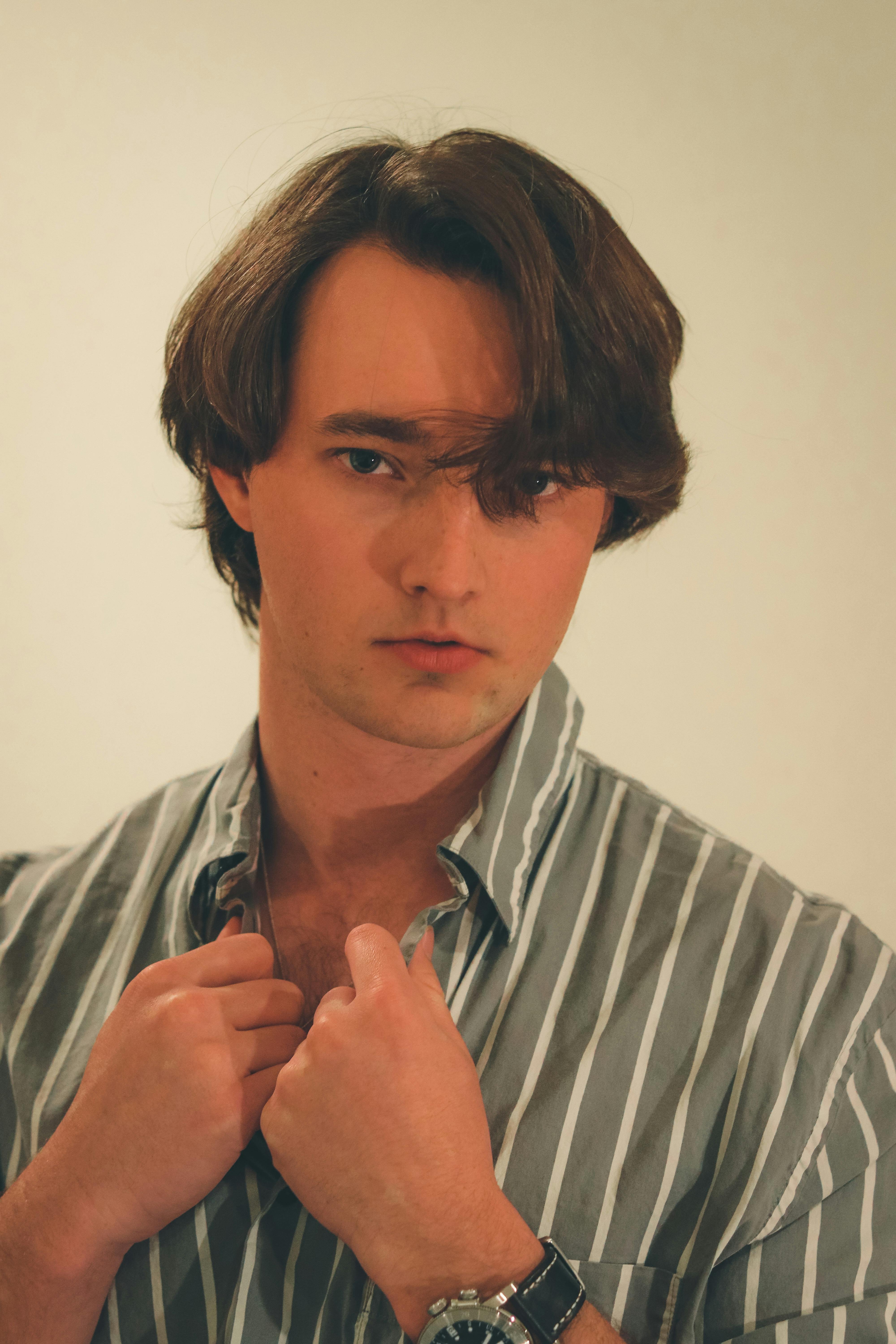 Portrait of a young man posing confidently in a striped shirt with a white studio background.