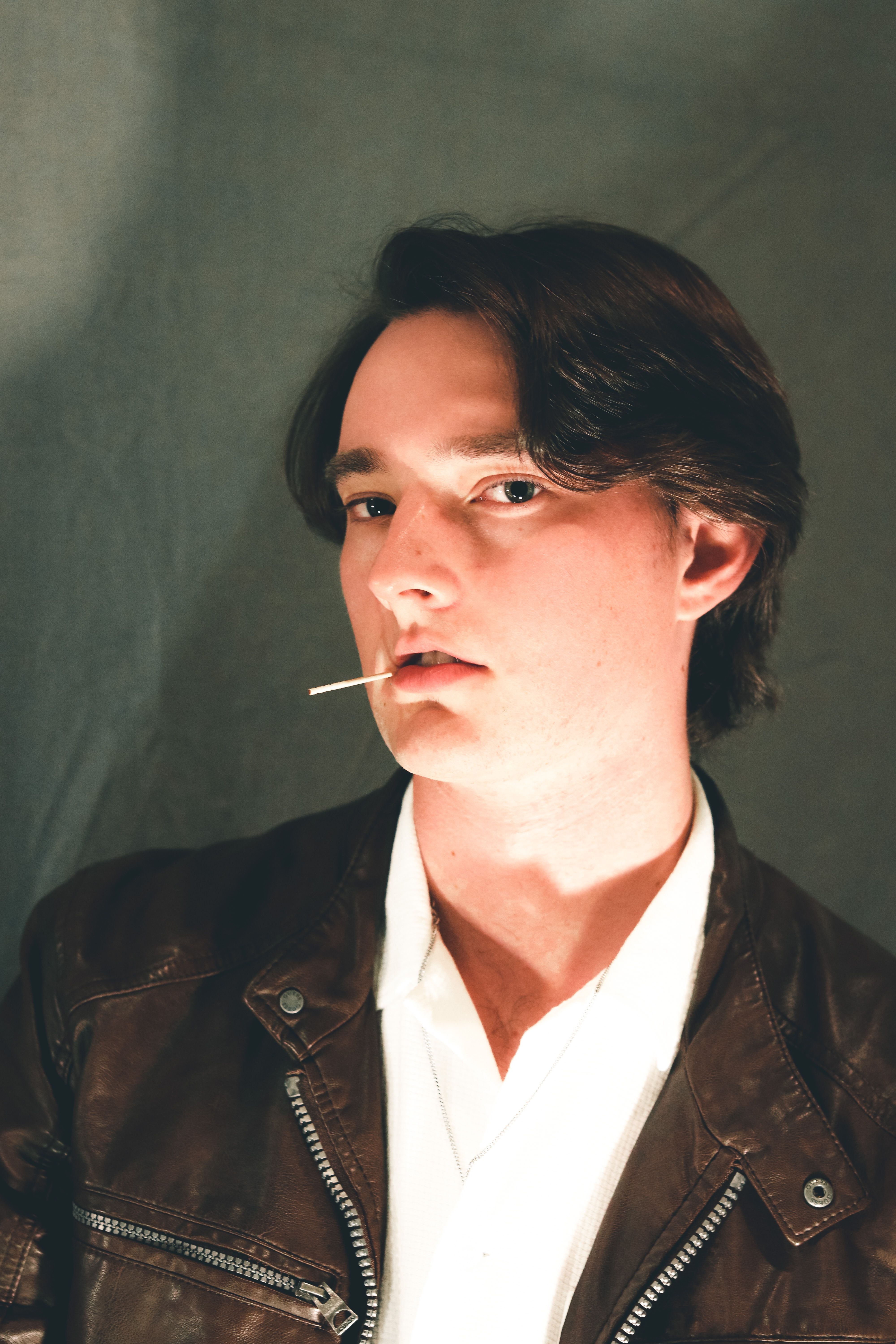 Stylish portrait of a man in a brown leather jacket with a toothpick, exuding cool confidence.