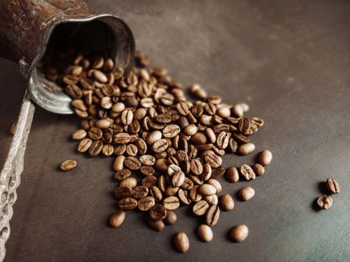 Free Close-up of roasted coffee beans spilled from a vintage copper pot, showcasing rich textures and warm tones. Stock Photo