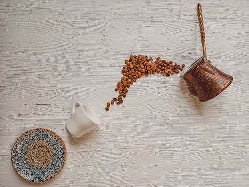 Coffee Beans Spilled on Wooden Surface with Cup and Saucer