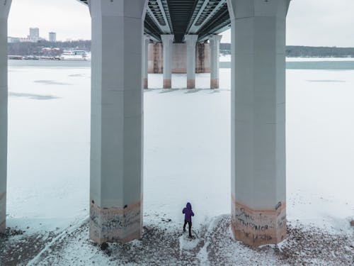 Snow on a River, and a Man Standing under a Massive Concrete Bridge