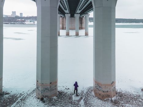 Person standing beneath bridge pillars on a snowy winter day in Novosibirsk.