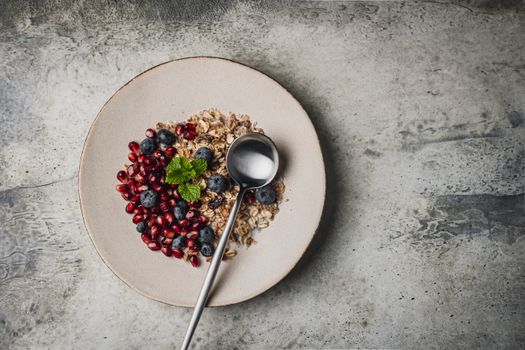 Top view of a healthy breakfast bowl with granola, blueberries, pomegranate seeds, and a spoon on a plate.