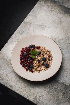 Top view of a healthy breakfast bowl with granola, pomegranate, blueberries, and mint on a concrete table.