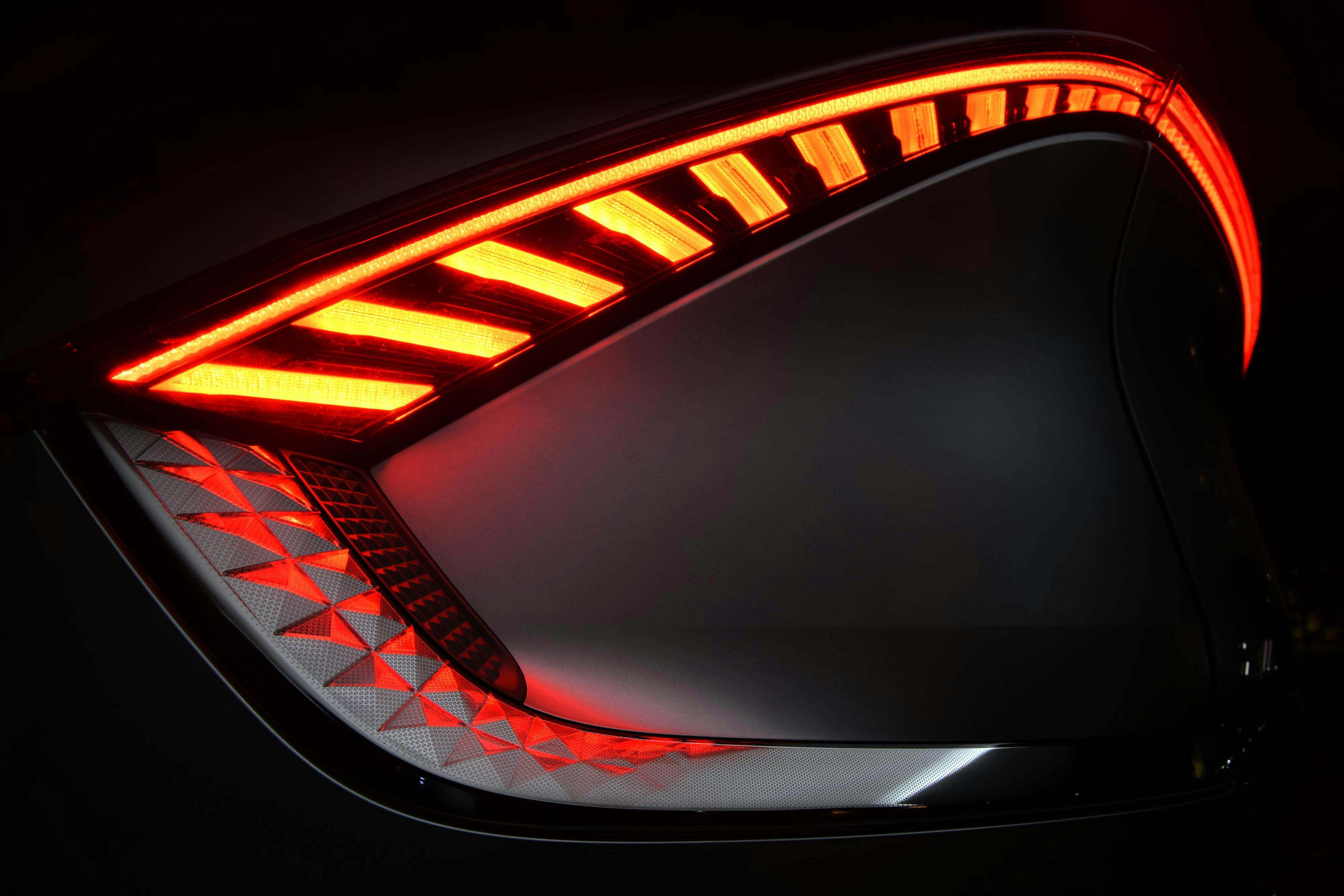 A close-up shot of a modern car's sleek red taillight illuminated at night.