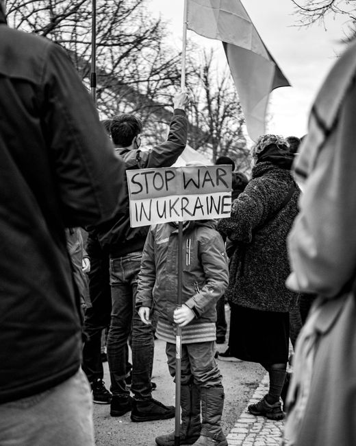 Grayscale protest in Berlin with child holding 'Stop War in Ukraine' sign.