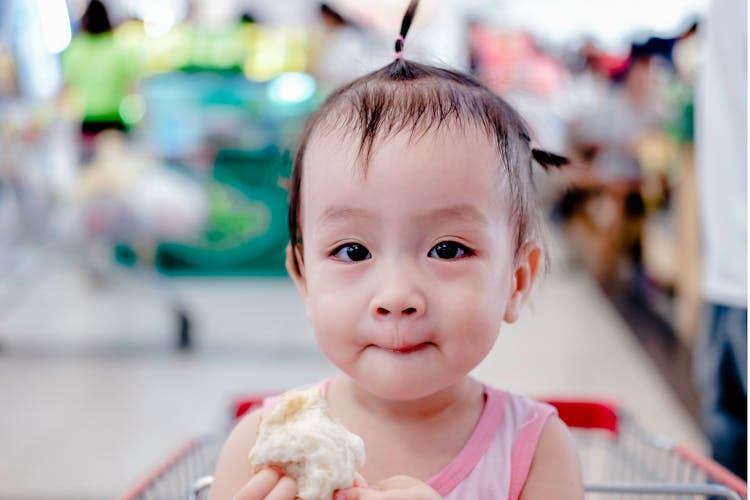 Cute Baby Girl Holding Bun In Shopping Cart