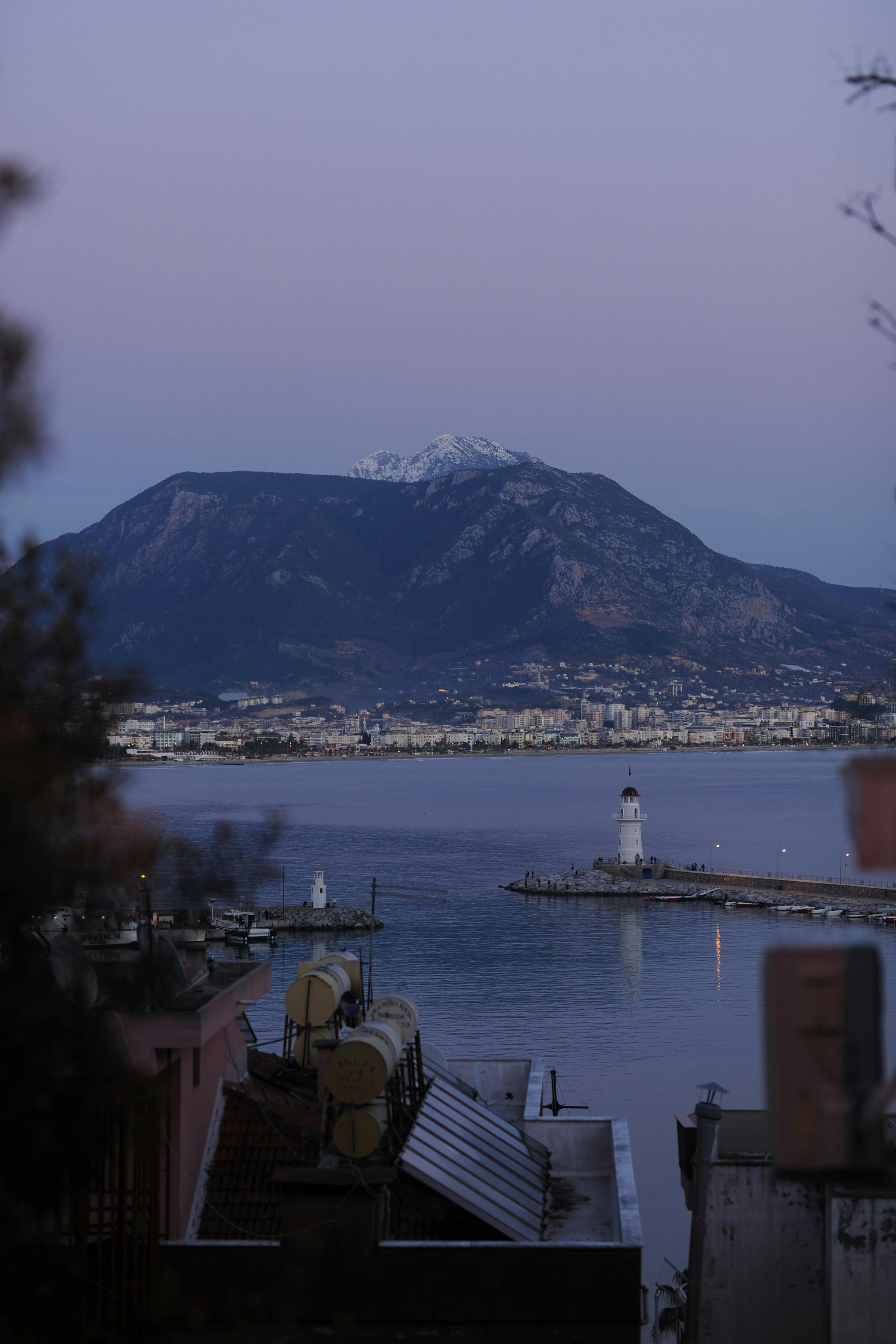 Stunning view of Alanya Lighthouse with mountains in the background at twilight, capturing the serene ambiance.