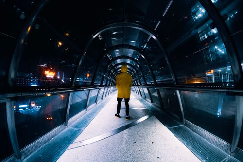 Free A person in a yellow jacket walks through a brightly lit tunnel at night, highlighting city lights. Stock Photo