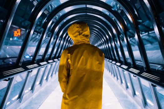 A person in a yellow jacket walks through a futuristic illuminated tunnel, showcasing urban symmetry.