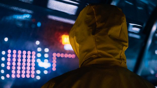 Person in yellow hoodie facing urban neon lights at night, an atmospheric cityscape.