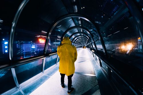 Free Man in yellow coat walking through a futuristic illuminated tunnel at night, showcasing urban architecture. Stock Photo