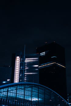Night view of illuminated skyscrapers with modern architectural design and cityscape lights.