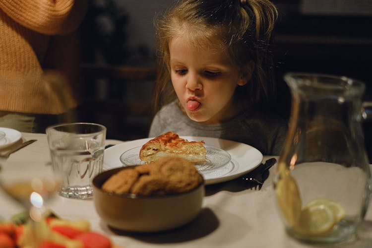 A Young Girl Looking At The Food On Ceramic Plate With Her Tongue Out