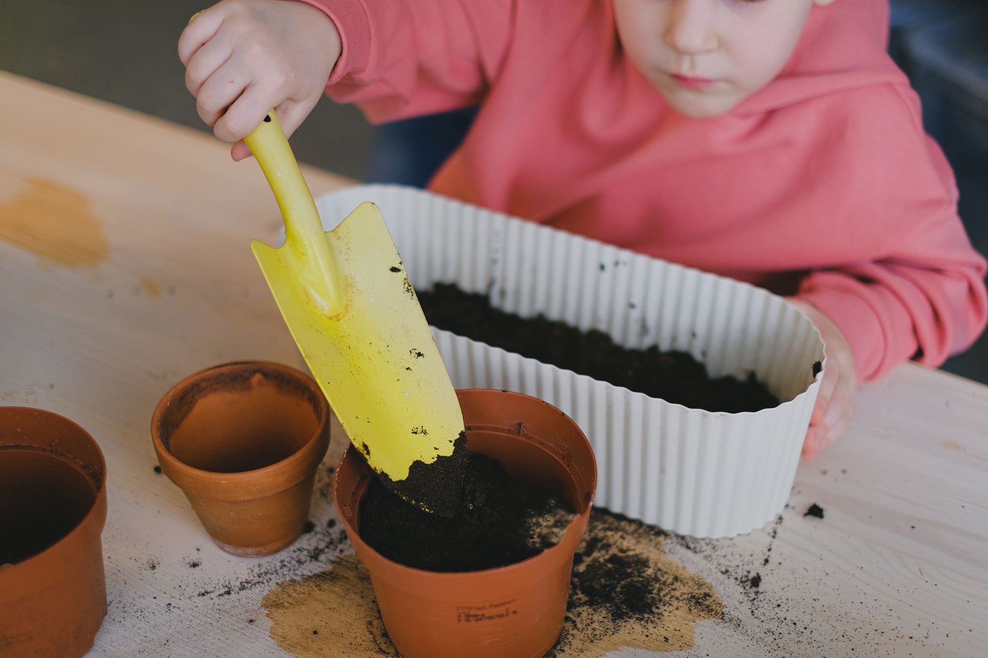 A Child Putting Soil in a Pot Using a Garden Trowel