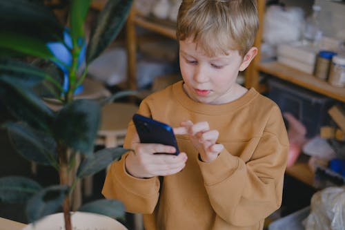 Free A Boy Wearing a Brown Sweater Using a Smartphone Stock Photo