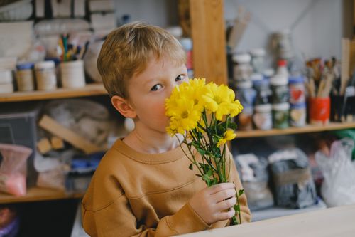 Free A young blond boy holds vibrant yellow flowers indoors with a creative background. Stock Photo