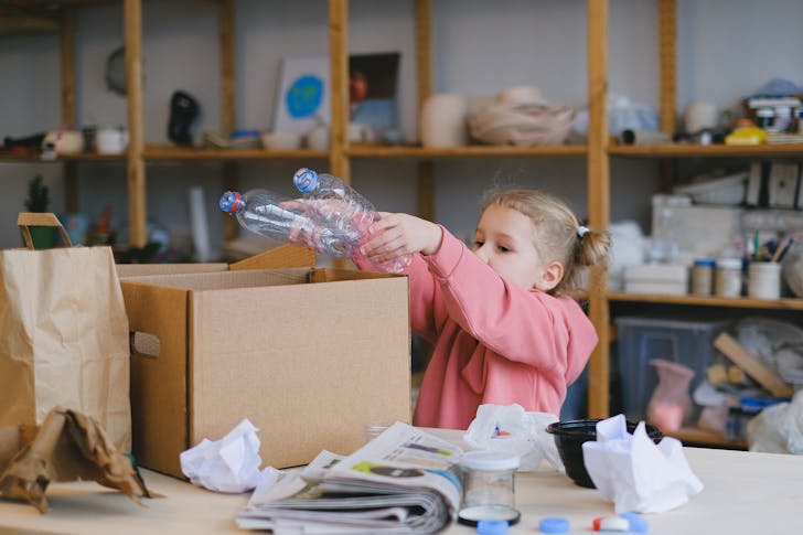 A Girl Putting Plastic Bottles on a Cardboard Box