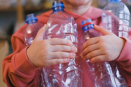Free A child in a pink hoodie holding multiple recyclable plastic bottles, emphasizing zero waste and sustainability. Stock Photo