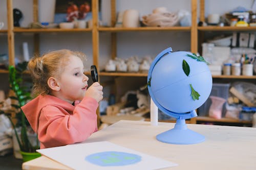 A Girl in Pink Hoodie Looking at a Globe Using a Magnifying Glass