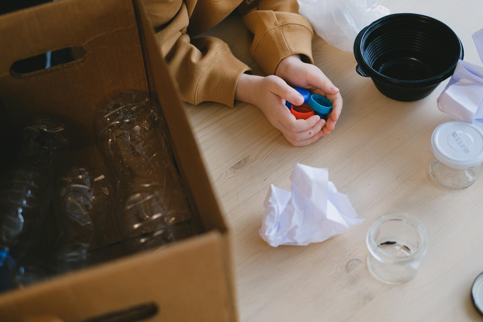 Person organizing recyclable materials like plastic lids and paper on a table.