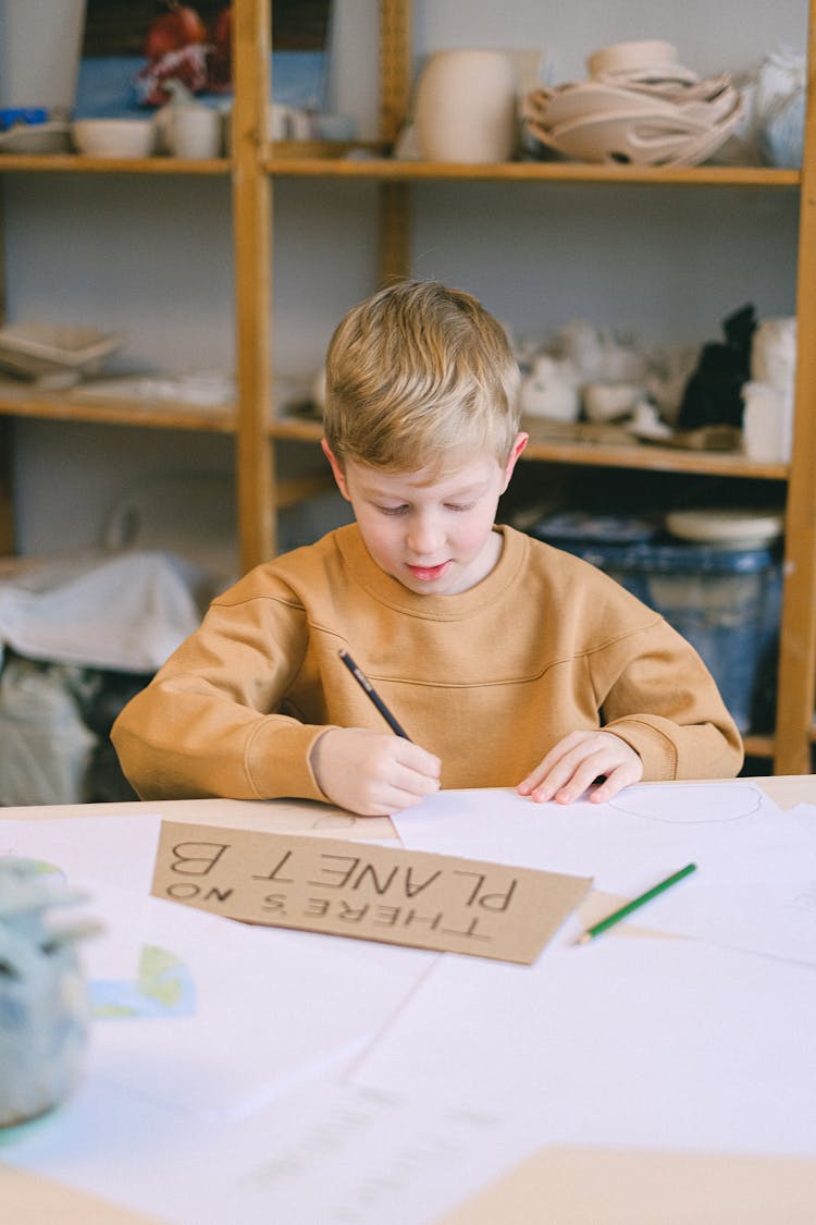 A Boy In Brown Sweater Writing On White Paper