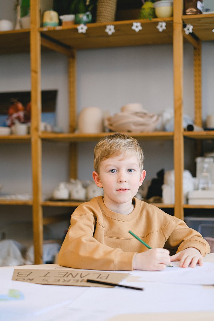 A Boy In Brown Sweater Writing On White Paper
