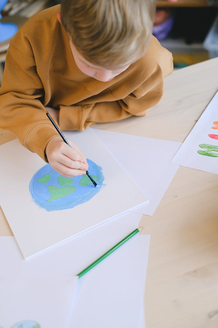 A Blond Boy Painting Earth On White Paper