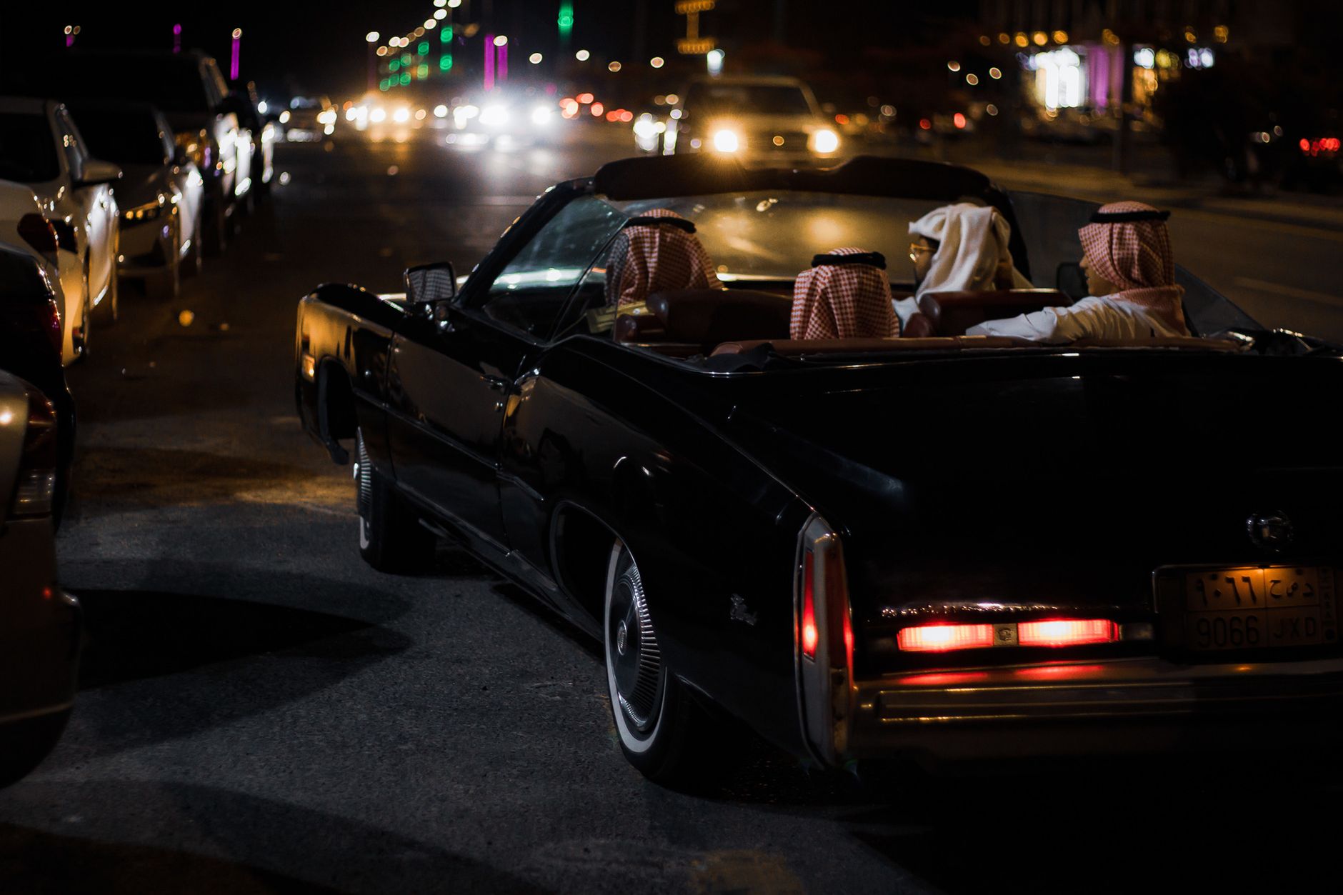 Classic convertible with passengers on a night drive through Saudi Arabian city streets.