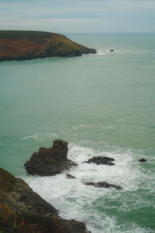 Free A stunning view of rocks and crashing waves on the scenic coastline under a cloudy sky. Stock Photo