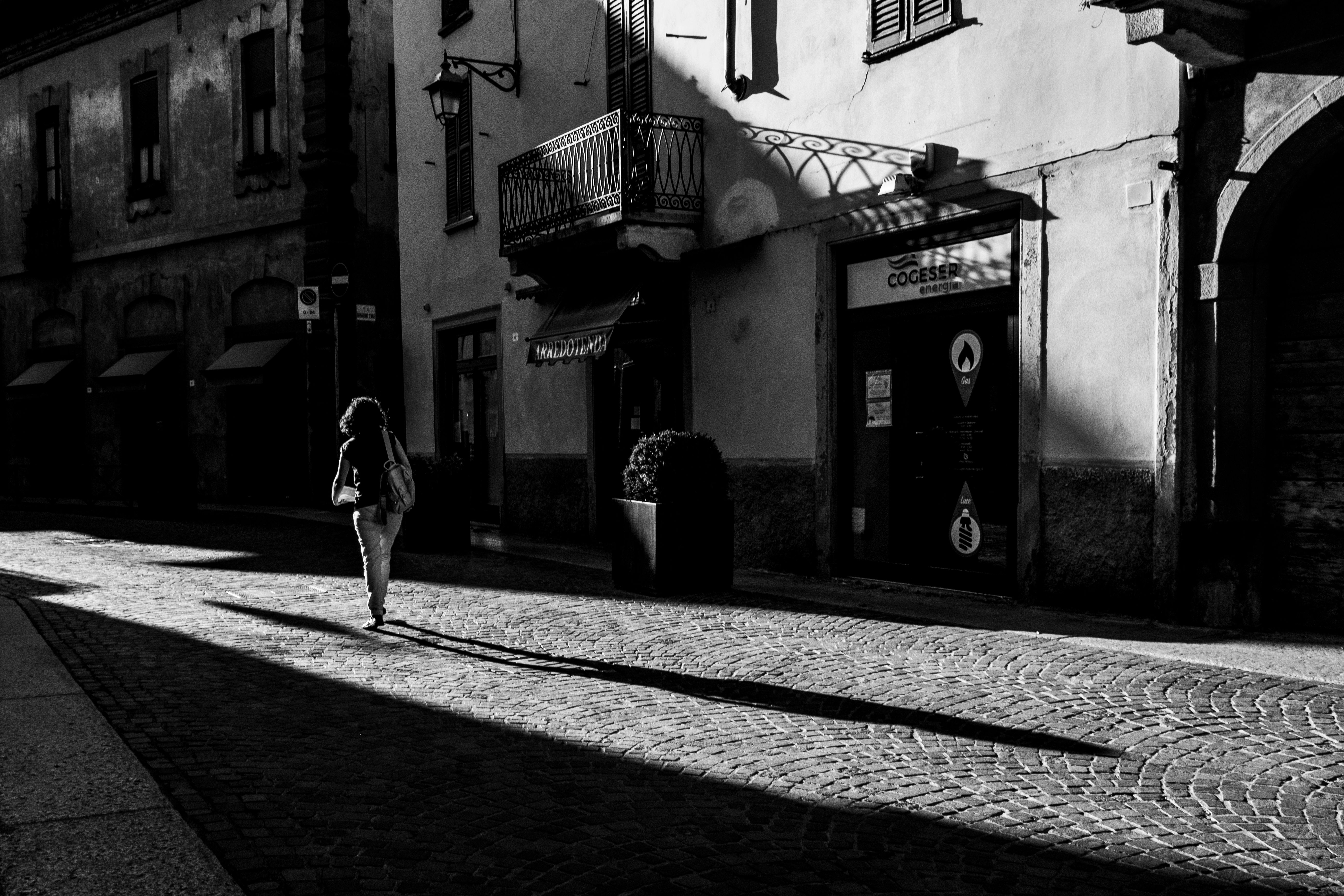 A woman walking on a cobblestone street in Treviglio, showcasing shadows and light.