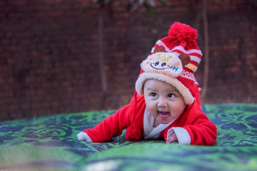 Free Cute baby in a red winter outfit and playful hat smiles happily indoors. Stock Photo