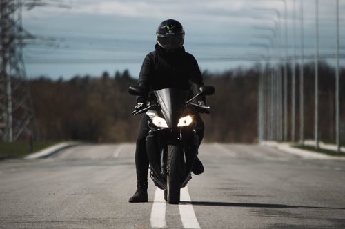 Free Motorcyclist riding fast on an open road, wearing black gear and helmet, outdoors. Stock Photo