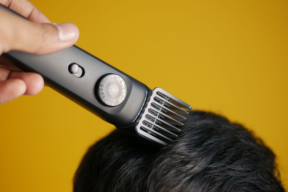 Close-up of an electric hair clipper trimming hair against yellow background.