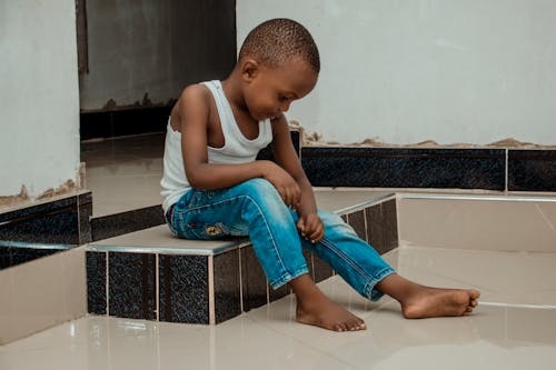 A Boy Sitting on the Floor while Looking at the Denim Pants He is Wearing