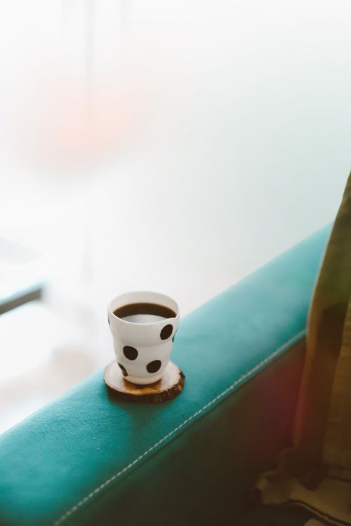 Free A stylish black polka dot coffee mug sits on a teal sofa armrest, creating a cozy ambiance. Stock Photo