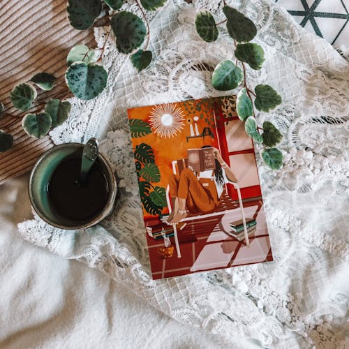 A Book Beside a Cup of Tea Surrounded with Green Leaves