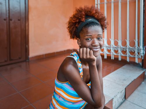 Free A cheerful woman with an afro hairstyle sitting on stairs, showcasing vibrant hair and a colorful dress. Stock Photo
