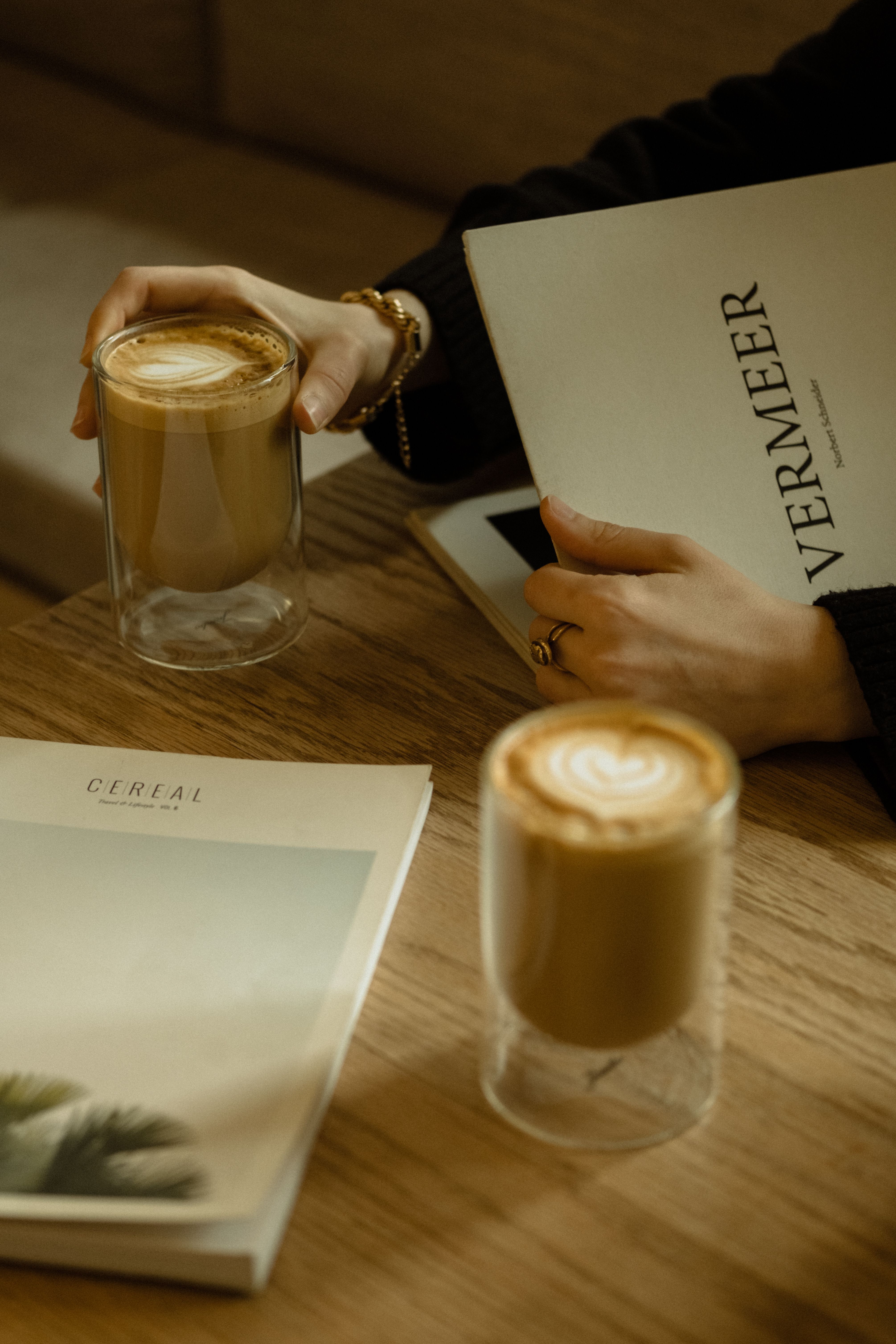 A warm, cozy scene of a woman enjoying coffee with books on a wooden table.